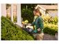 Femme taillant une haie avec un taille-haie, portant des lunettes de sécurité et des gants.