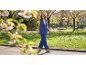 Femme en gilet bleu et pantalon assorti marchant dans un parc fleuri.