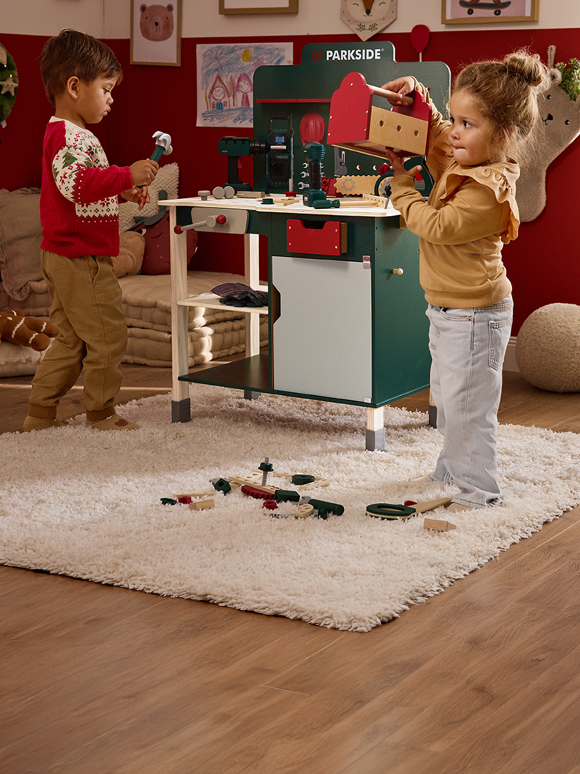 Deux enfants jouent avec un établi jouet Parkside et des outils en bois.
