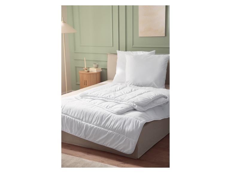Couette matelassée blanche et oreillers sur un lit, intérieur de chambre avec mur vert.