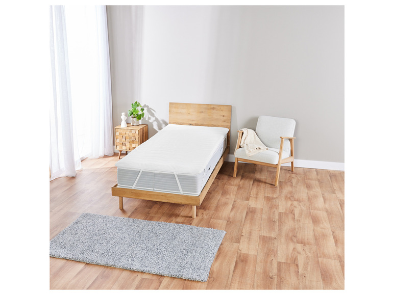 Un lit avec un protège-matelas et un tapis.