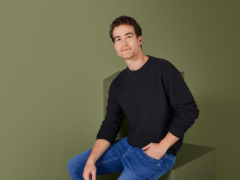 Homme en pull noir et jean bleu.