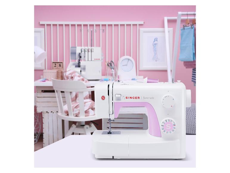 Machine à coudre blanche avec des accents roses sur une table dans une pièce de couture rose.
