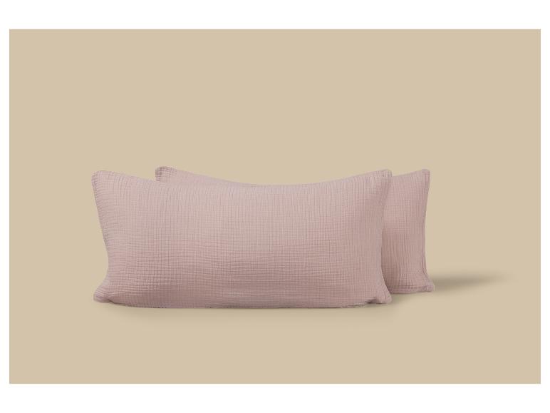 Deux oreillers rectangulaires rose pâle en tissu gaufré sur fond beige.