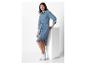 Une femme porte une robe en jean bleue avec une ceinture et des baskets blanches.