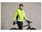 Un homme avec une veste de vélo jaune vif et des gants noirs se tient à côté d'un vélo noir.