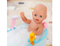 Poupée dans le bain moussant, jouant avec un canard jaune.