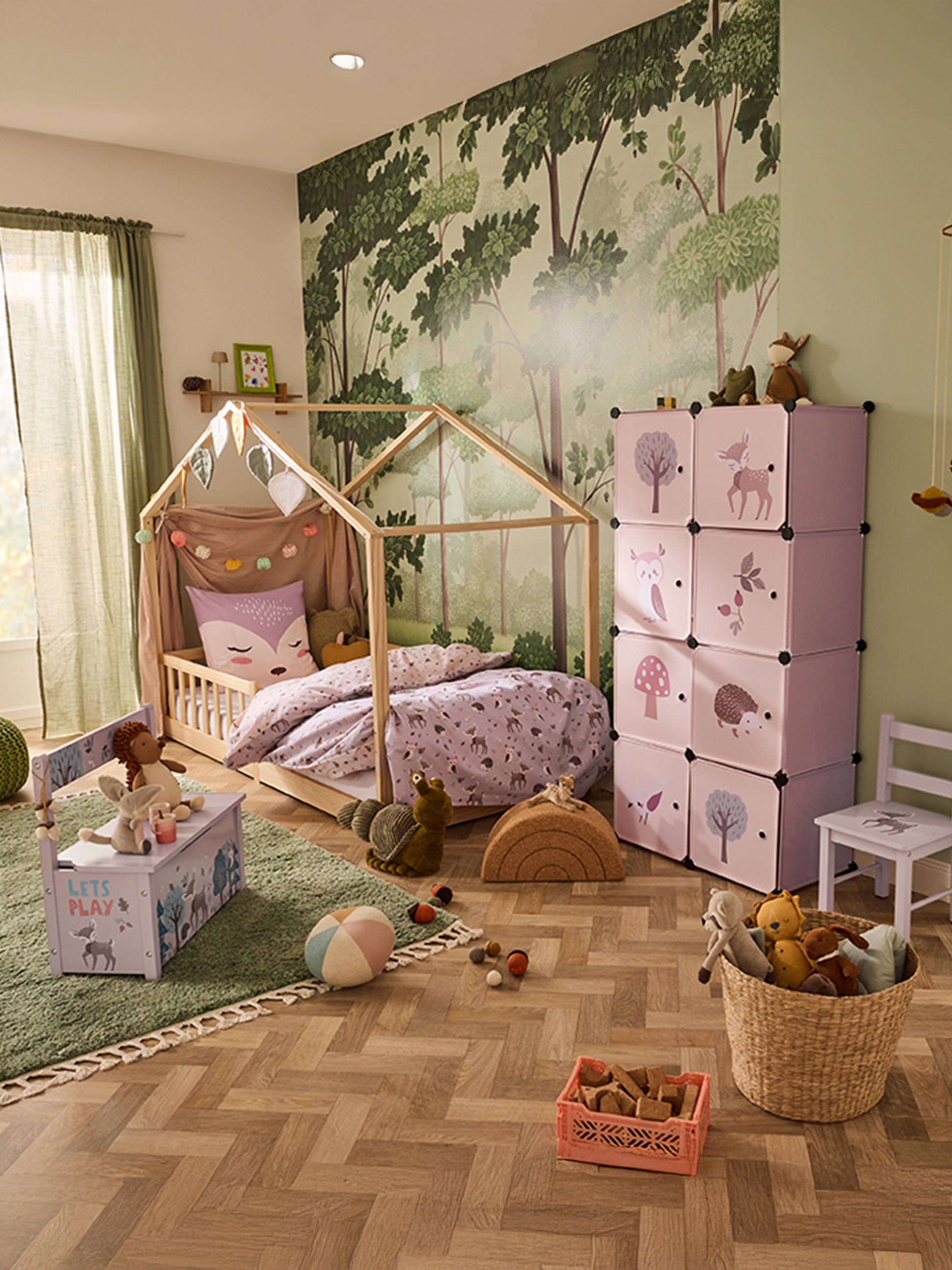 Chambre d'enfant avec lit cabane, cubes de rangement roses et papier peint forêt.