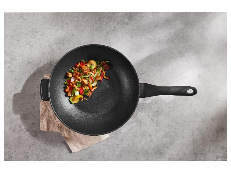 Wok noir avec un sauté coloré de tofu et de légumes sur une surface grise.