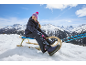 Fille en combinaison de ski et bonnet, assise sur une luge en montagne enneigée.