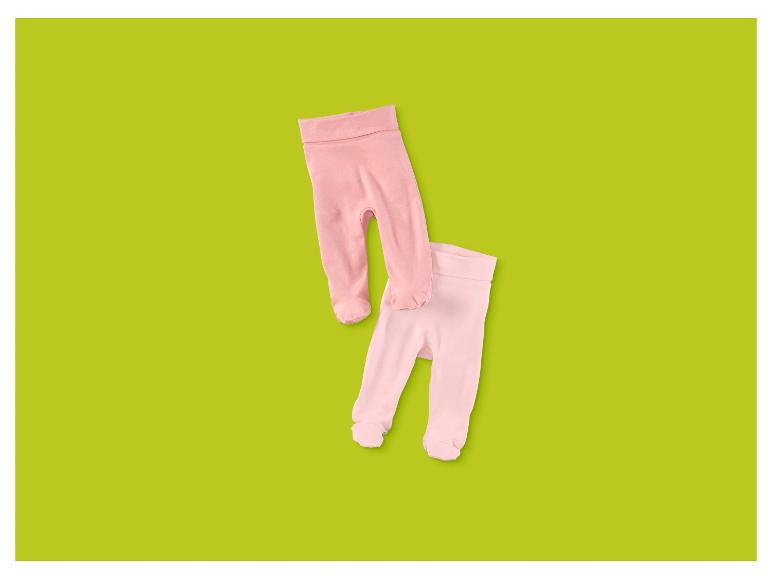 Deux paires de pantalons de bébé roses avec pieds sur fond vert.