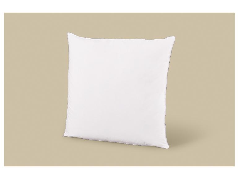 Oreiller carré blanc avec passepoil gris sur fond beige.