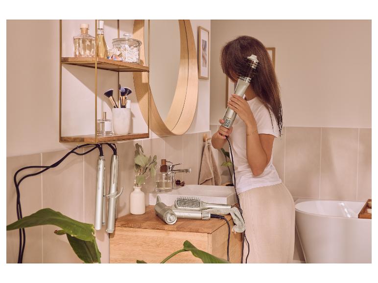 Femme se séchant les cheveux avec une brosse soufflante dans une salle de bain avec des produits capillaires.