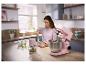 Femme cuisine dans une cuisine avec un robot pâtissier et un hachoir roses.