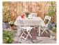 Table et chaises pliantes blanches, nappe beige, pour extérieur.