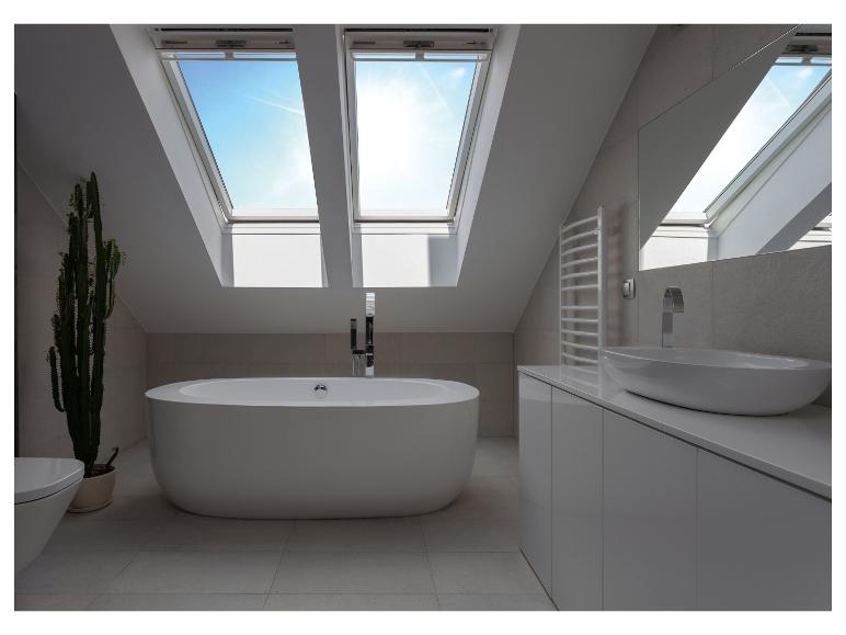 Salle de bain moderne sous les combles avec baignoire îlot, lavabo et fenêtres de toit.