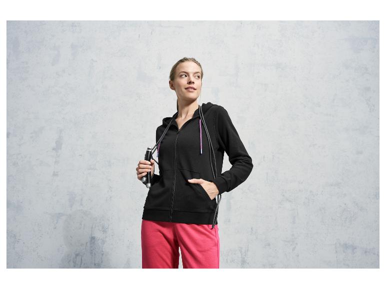Une femme portant un sweat à capuche noir et un pantalon rose avec une corde à sauter.
