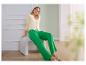 Femme en cardigan jaune et pantalon vert, assise sur un tabouret blanc.