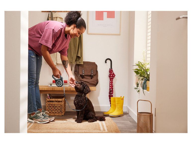Une femme avec son chien, une laisse rétractable et des baskets vertes dans un couloir.