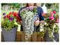 Femme tenant une jardinière grise avec des fleurs colorées, entourée de jardinières similaires.
