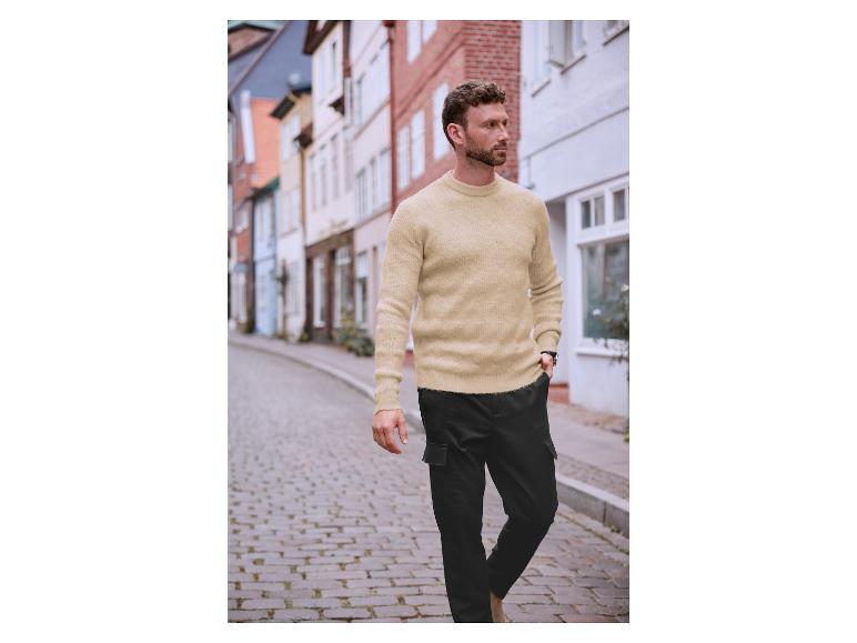 Un homme porte un pull beige et un pantalon cargo noir dans une ville.