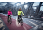 Deux personnes en vestes de cyclisme réfléchissantes et casques à vélo électrique sur un pont.