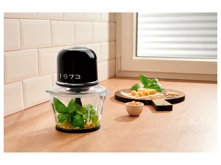 Hachoir noir avec ingrédients pour pesto sur planche en bois dans la cuisine.