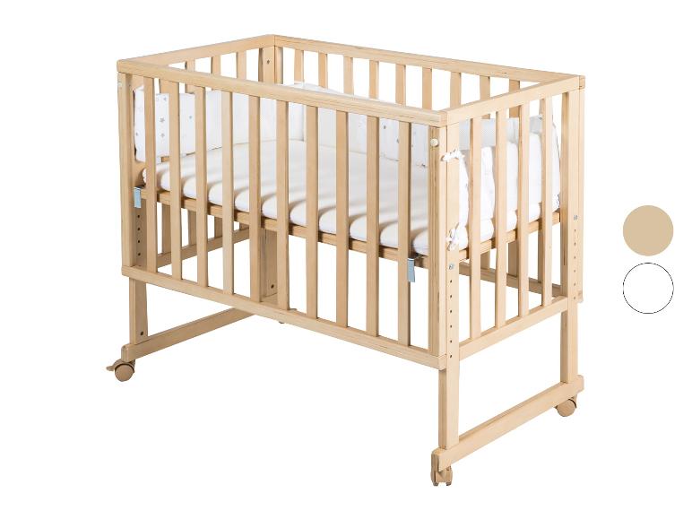 Lit bébé en bois clair avec literie blanche et roulettes.