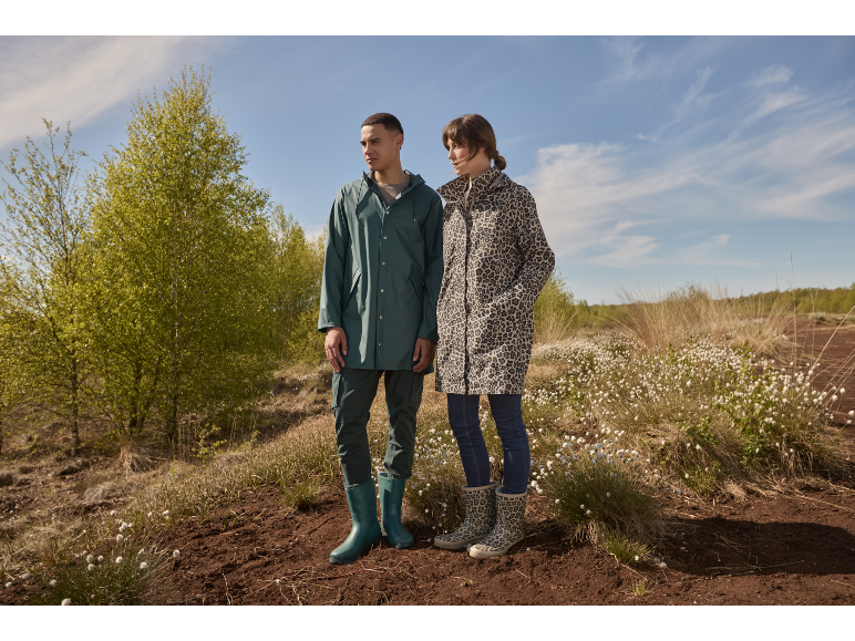 Homme et femme en imperméables et bottes dans un champ de fleurs blanches.