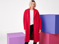 Une femme portant un manteau rouge se tient devant des blocs de couleurs.