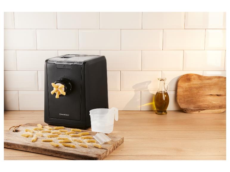 Machine à pâtes noire avec des pâtes fraîches sur une planche en bois.