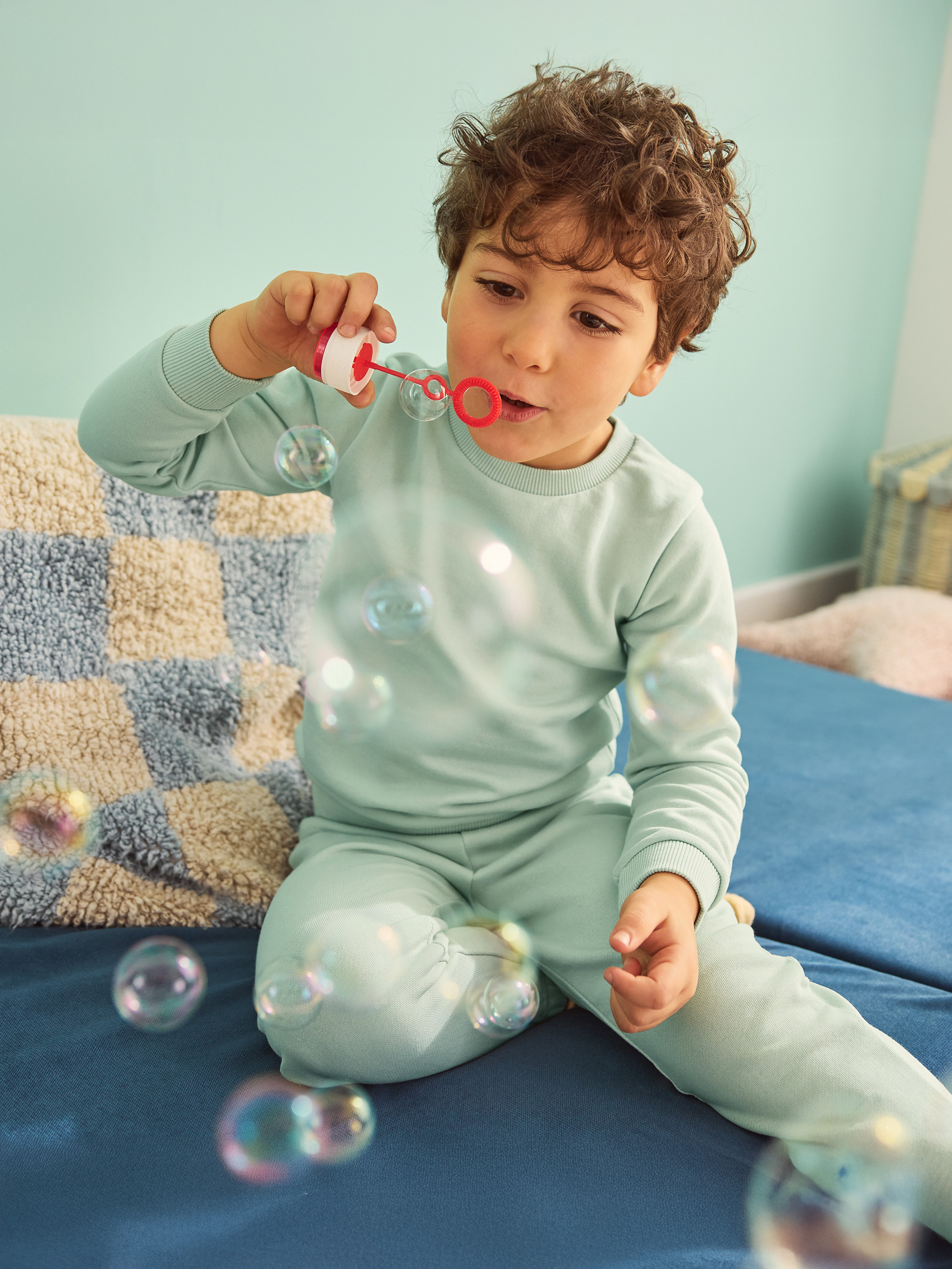 Garçon en pyjama bleu soufflant des bulles sur un canapé bleu.
