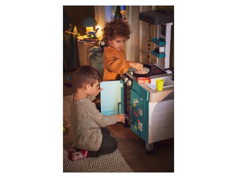Deux enfants jouent à cuisiner avec une cuisine en plastique avec un four, une cuisinière et un réfrigérateur.