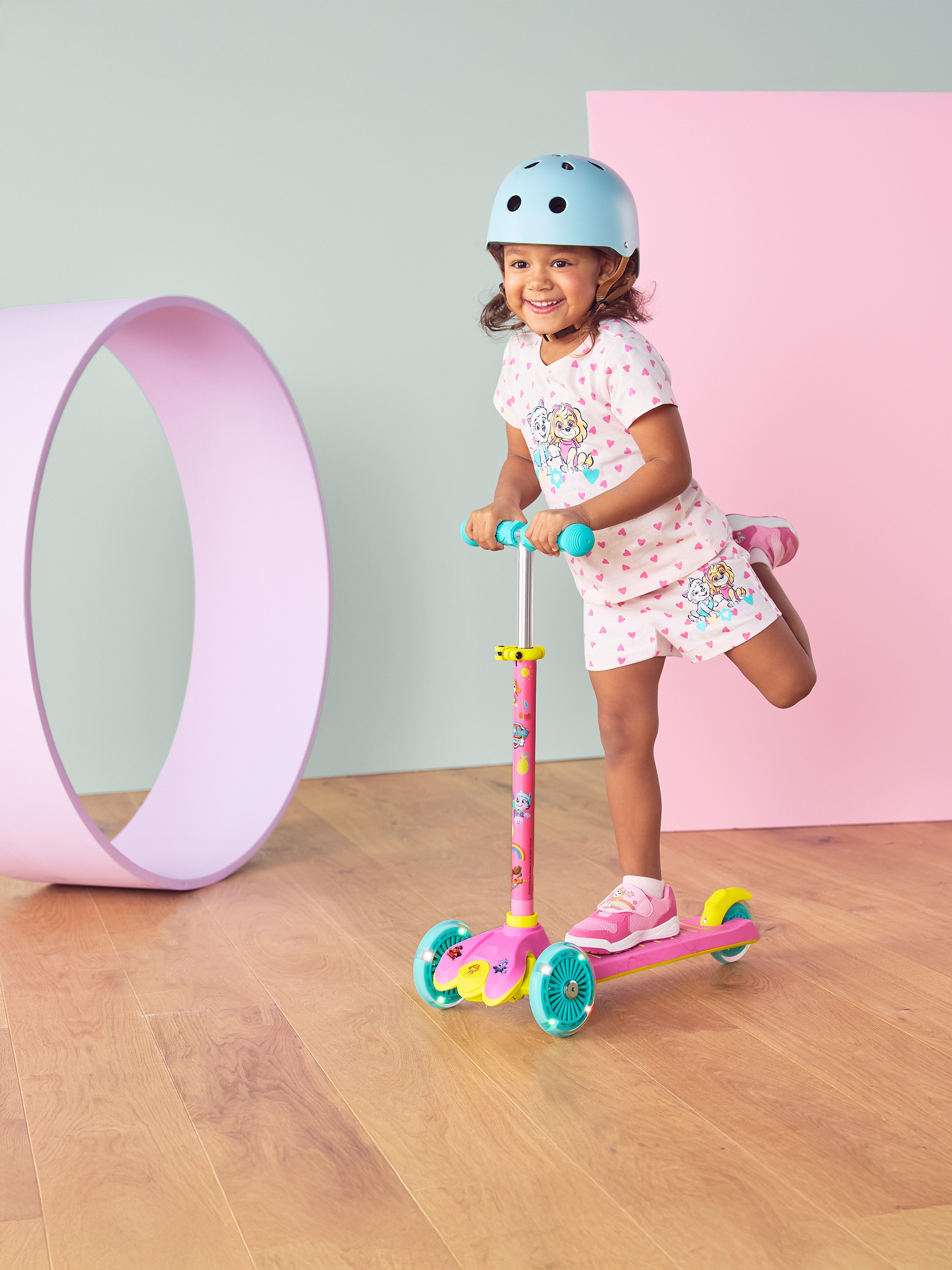 Fille avec casque et trottinette rose à roues lumineuses, souriante.