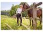Femme en chemise blanche et pantalon foncé avec cheval près d'une clôture en bois à la campagne.
