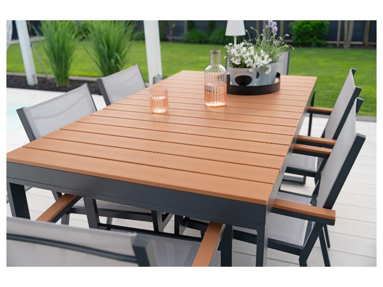 Ensemble de salle à manger extérieur avec table en bois et chaises grises sur une terrasse, avec verdure en arrière-plan.