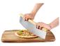 Mains coupant une pizza avec une grande roulette à pizza sur une planche en bois.