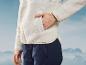 Une femme portant une veste crème et un pantalon bleu sur fond de montagnes.