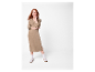 Femme aux longs cheveux roux posant en robe marron et baskets blanches.