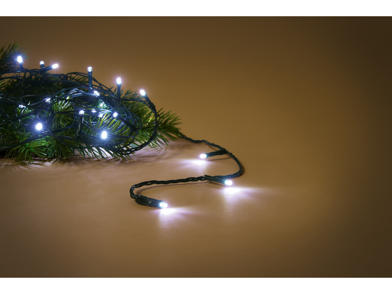 Guirlande lumineuse LED blanche sur une branche de sapin verte, sur fond marron chaud.