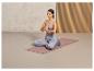 Une femme médite en position du lotus sur un tapis de yoga rose avec un coussin de méditation.