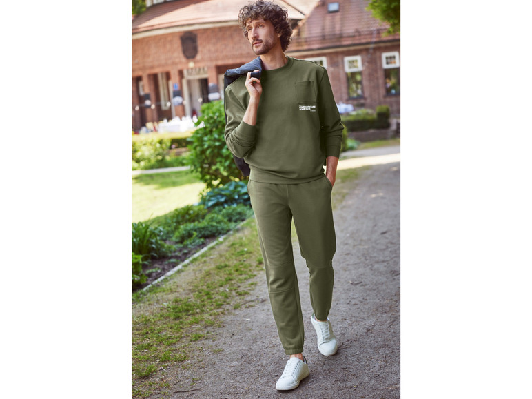 Un homme portant un sweat-shirt et un pantalon de survêtement verts avec des baskets blanches.
