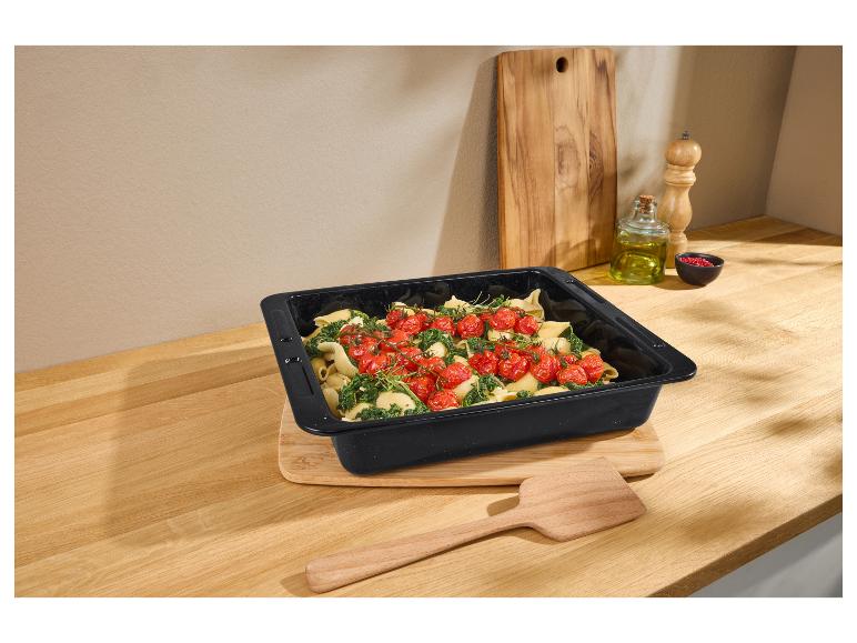 Plat de cuisson noir avec pâtes, épinards et tomates cerises sur un comptoir en bois.