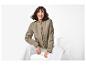 Femme souriante en blouson bomber kaki et pantalon blanc, assise sur une chaise blanche.