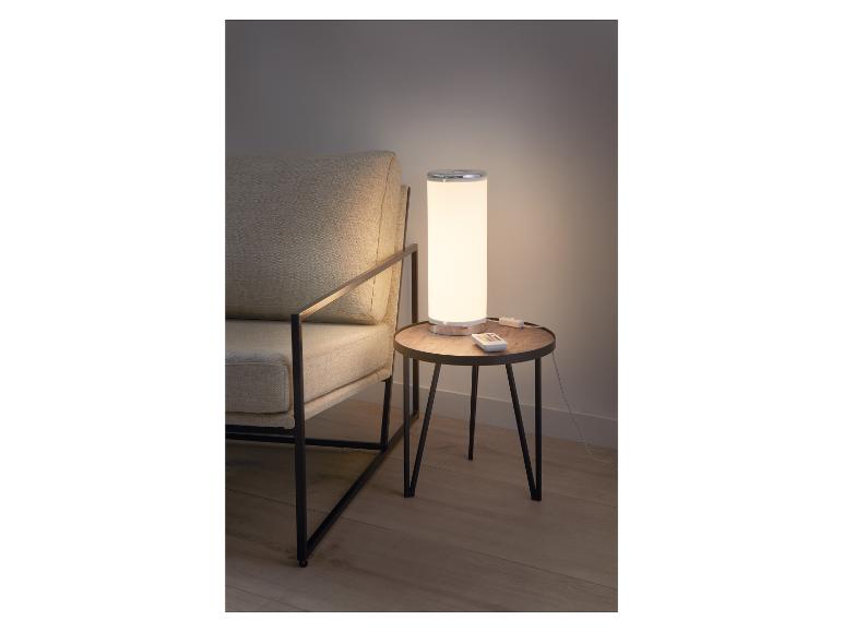Lampe de table avec télécommande sur une table en bois à côté d'un fauteuil.