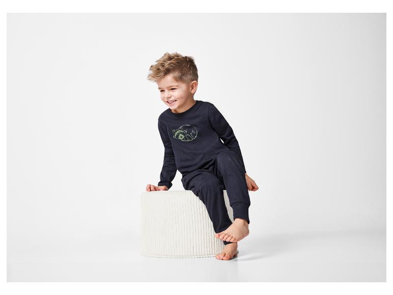 Un jeune garçon en pyjama bleu marine est assis sur un tabouret blanc.