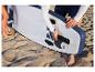 Un homme installe un aileron sur le stand up paddle bleu HOME DELUXE Moana sur la plage.