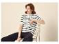 Femme en cardigan rayé noir et blanc et pantalon noir, assise sur une chaise.