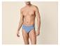 Homme en slip de coton bleu, posant sur un fond beige.