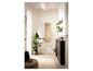 Hall d'entrée avec meuble à chaussures, miroir, porte-manteau, étagères et grande plante verte.